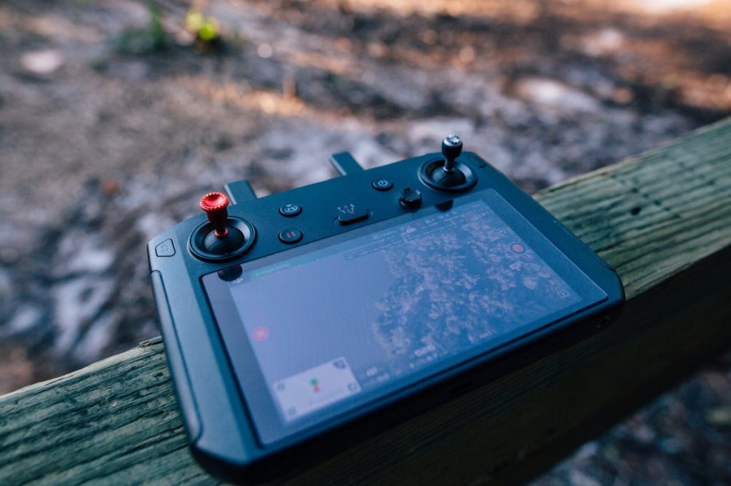 Close-up of a drone controller with visible screen, resting on a wooden surface outdoors.